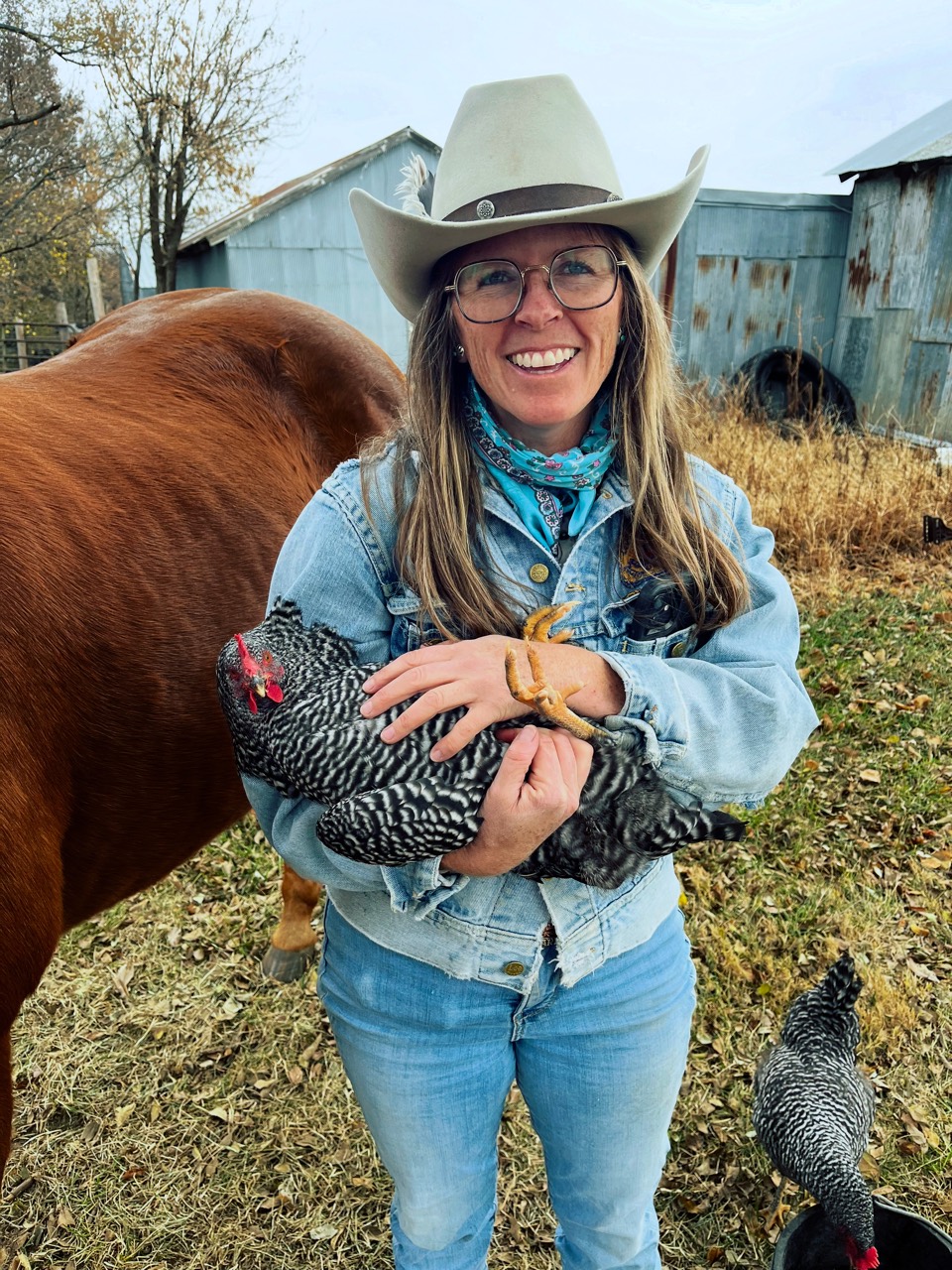 Mandy smiling while holding a chicken beside a horse