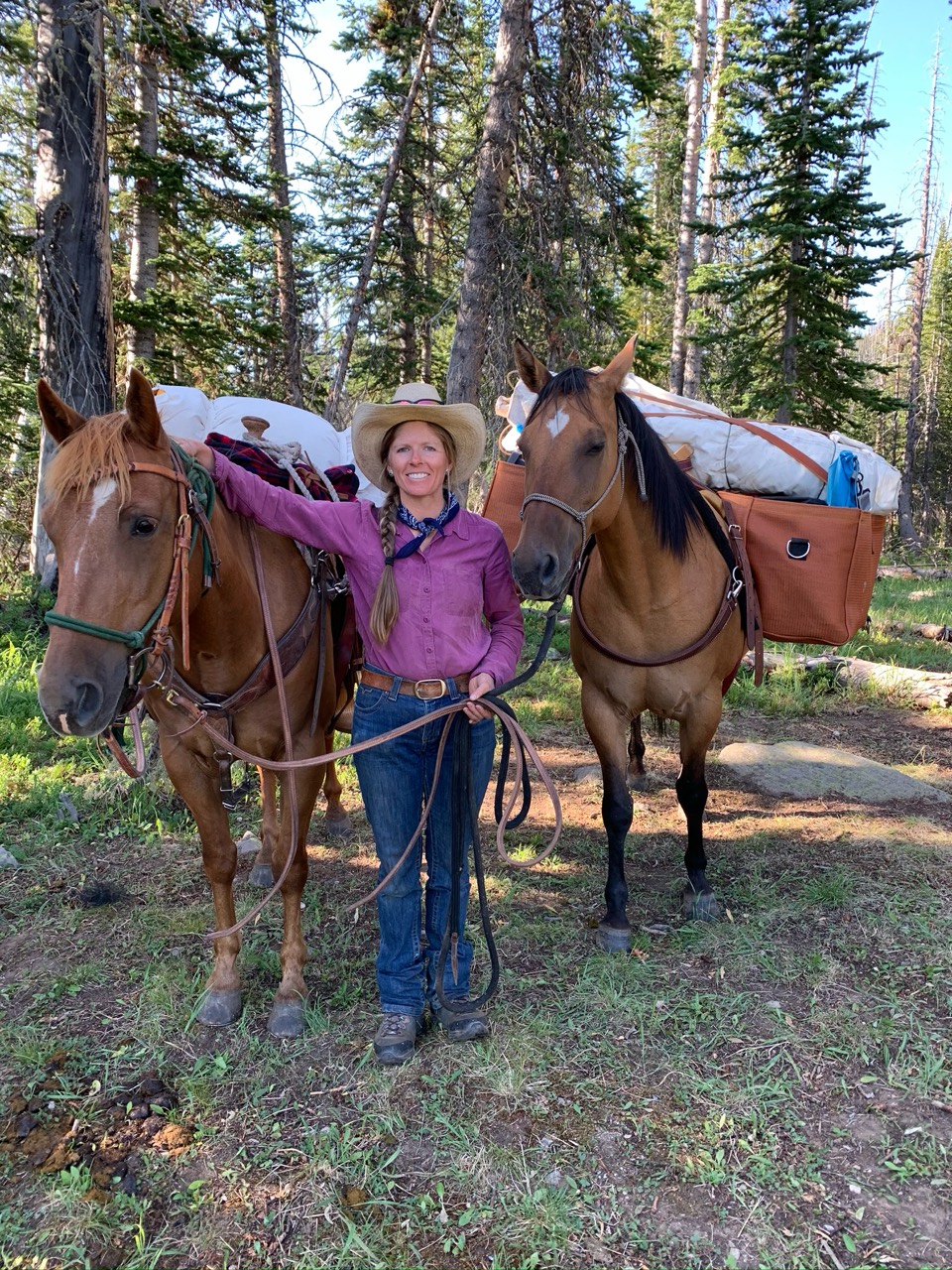 Mandy standing between two packed horses in the mountains